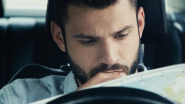 pensive man looking at map while sitting in car and estimating route