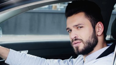 young and confident man driving car and looking at camera