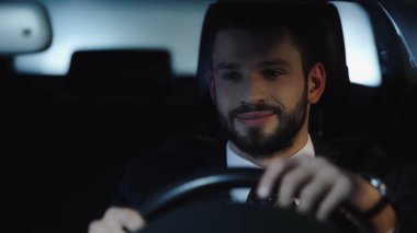 smiling bearded businessman driving car in evening