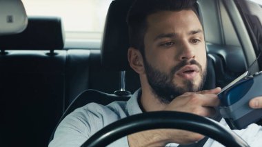 young man paying through credit card reader while sitting in car