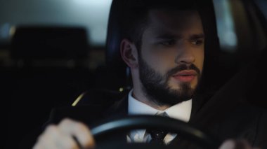 young businessman looking aside while driving car at night