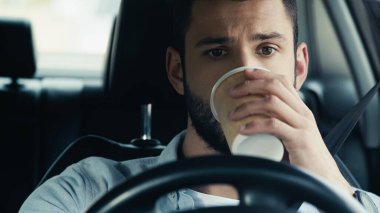 young man driving car and drinking coffee from paper cup