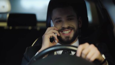 cheerful businessman driving car during conversation on smartphone