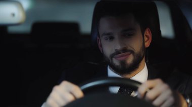young positive businessman in formal wear driving car at night