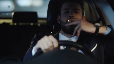 young businessman smoking while driving car in late evening