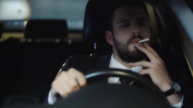 bearded businessman smoking cigarette while driving auto at night