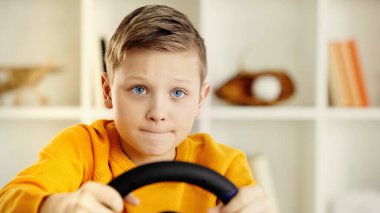 focused schoolboy holding toy steering wheel and playing video game