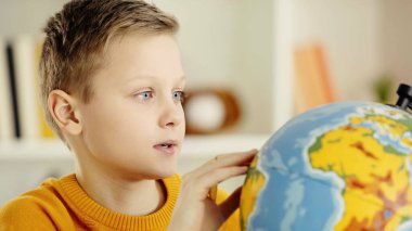 schoolboy with blue eyes looking at globe while exploring world 