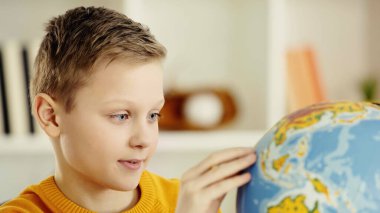 preteen boy with blue eyes looking at globe while exploring world at home 