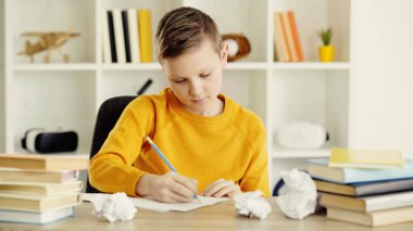 preteen schoolboy drawing near crumpled papers and books on desk 