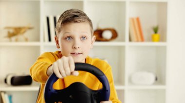 tensed schoolboy holding toy steering wheel and playing video game