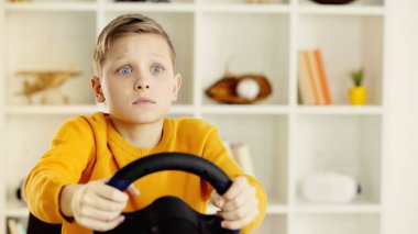 sad schoolboy holding toy steering wheel and playing video game