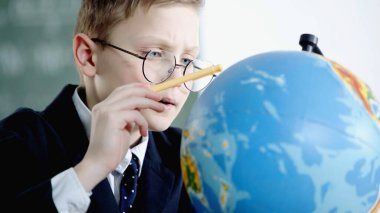 schoolboy in glasses pointing with pencil at globe in classroom 