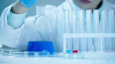 partial view of blurred scientist adding red sample into test tube in laboratory 