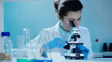 scientist in white coat making analysis while looking through microscope in clinical laboratory