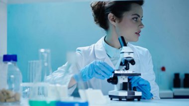 scientist in white coat making analysis near microscope in clinical laboratory