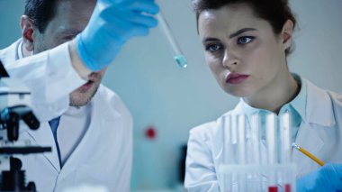 two scientists in white coats looking at test tube with sample in laboratory