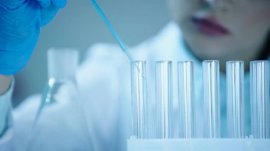 partial view of blurred scientist adding blue liquid into clean test tube in laboratory 