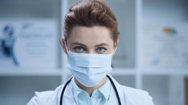 female doctor in medical mask looking at camera in clinic 