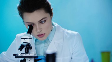 female scientist in white coat looking through microscope in clinic