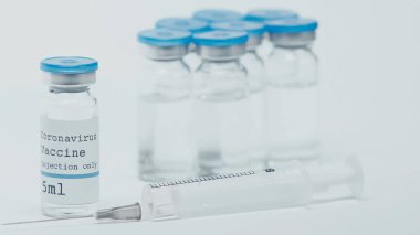 close up of syringe near bottles with coronavirus vaccine and lettering isolated on white