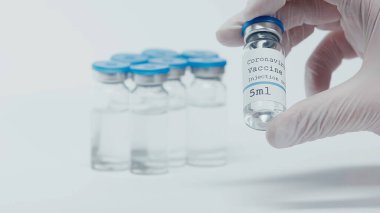 cropped view of person taking bottle with coronavirus vaccine liquid on white 