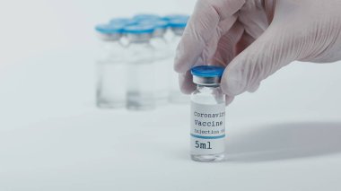 cropped view of person holding bottle with coronavirus vaccine liquid on white 