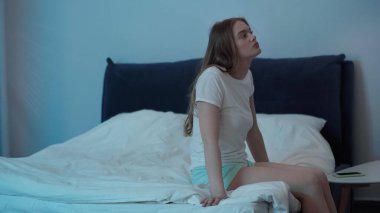 Young woman sitting on bed while suffering from insomnia at night