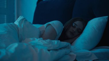 Young woman sleeping on white bedding in bedroom at night