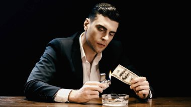 Businessman burning dollar banknote near ashtray isolated on black 