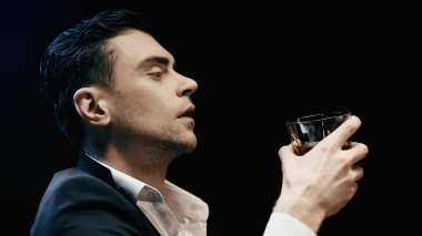 Side view of businessman in suit holding glass of whiskey isolated on black 