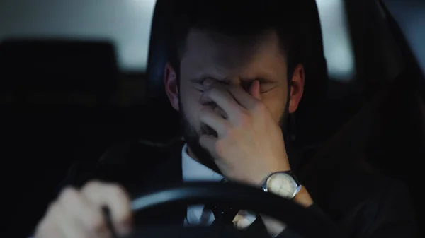 sleepy businessman touching eyes while driving car in evening