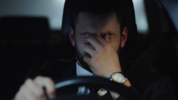 sleepy businessman touching eyes while driving car in evening