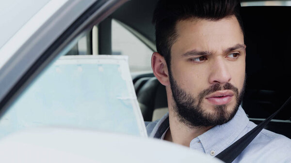 young bearded man looking away while sitting in car with map