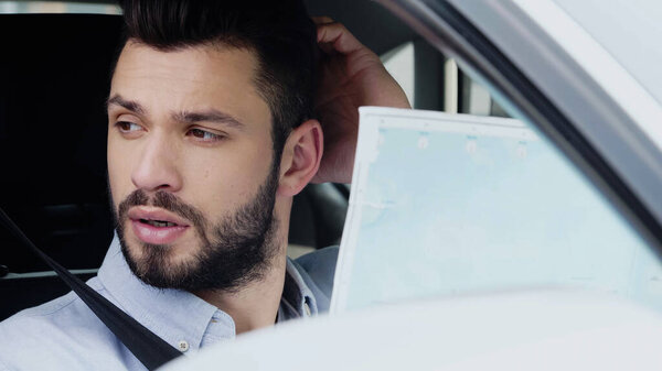 young man touching head and thinking while sitting in car with map