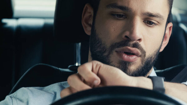 surprised and discouraged man looking at wristwatch while driving car