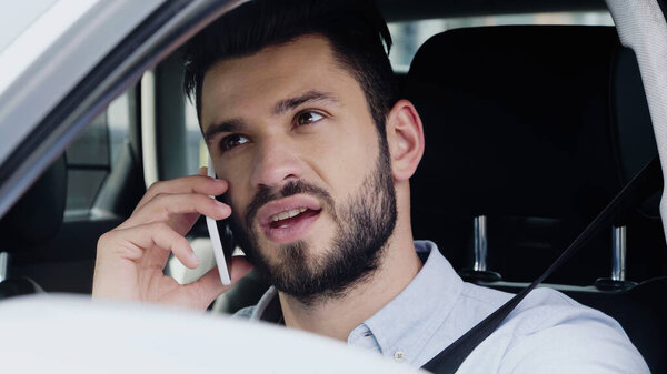 young man talking on cellphone and looking away while driving automobile