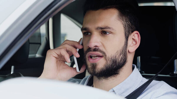 young man looking ahead and talking on cellphone while driving automobile