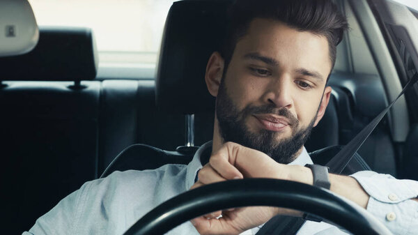 displeased bearded man driving car and looking at wristwatch