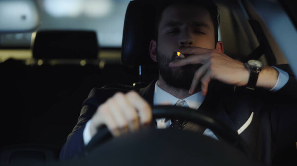 young businessman smoking while driving car in late evening