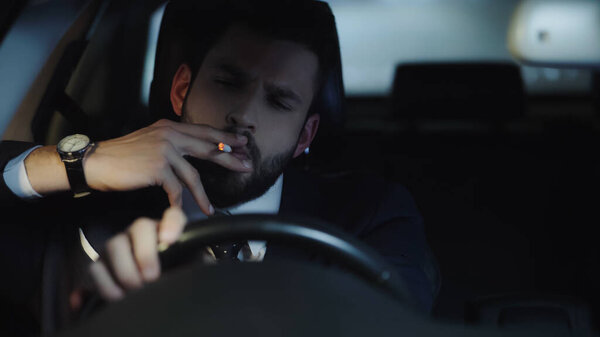 businessman in formal wear smoking cigarette and driving car at late night