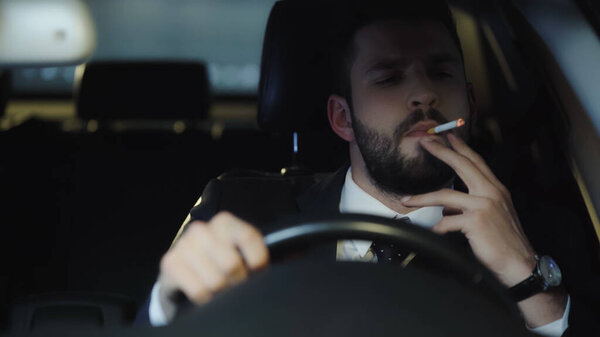 bearded businessman smoking cigarette while driving auto at night