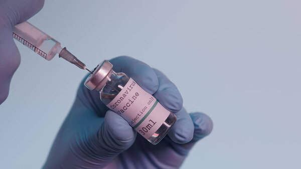 cropped view of scientist in latex gloves filling in syringe with vaccine from bottle with lettering isolated on grey 
