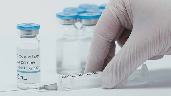 cropped view of person taking syringe near bottles with vaccine isolated on white 