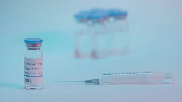 syringe near bottles with coronavirus vaccine and lettering on blue