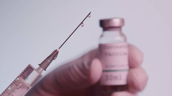 cropped view of scientist holding syringe and blurred bottle with vaccine isolated on grey 