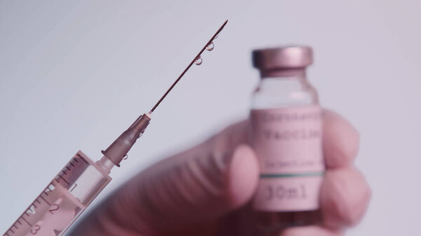 cropped view of scientist holding syringe with vaccine and blurred bottle isolated on grey 