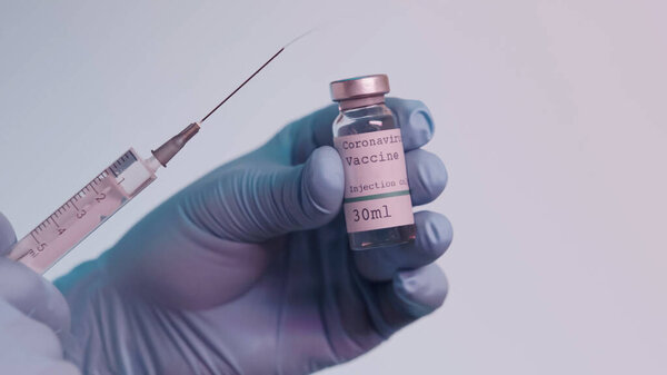 cropped view of scientist in latex gloves holding syringe and bottle with vaccine isolated on grey 