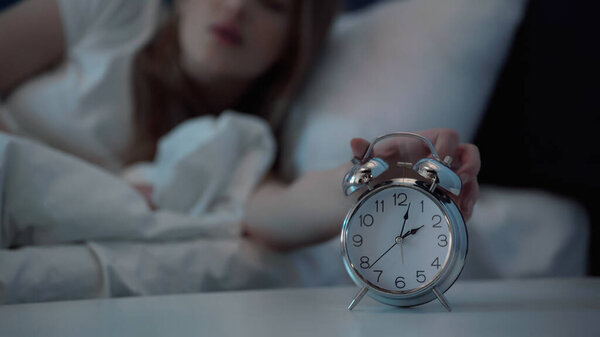 Cropped view of blurred woman turning off alarm clock in bedroom at night 