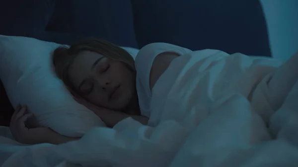 Young woman sleeping on white bedding at night